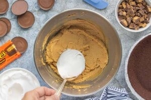 Spoonful of whipped topping being added to a peanut butter cheesecake mixture in a large mixing bowl.