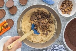 Chopped peanut butter cups being folded into a bowl of creamy peanut butter cheesecake filling.