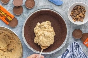 Spoonful of creamy peanut butter cheesecake filling being added to a prepared chocolate cookie pie crust.