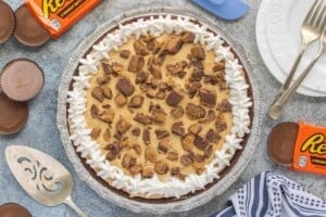 Overhead view of a no-bake chocolate peanut butter cup cheesecake in a chocolate cookie crust, topped with whipped topping and chopped peanut butter cups.