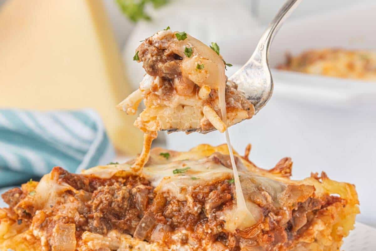 Fork lifting a bite of cheesy spaghetti pie casserole filled with ground beef, pasta sauce, and tender spaghetti noodles.