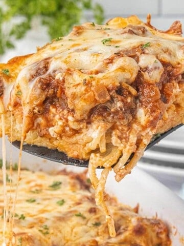 Cheesy slice of spaghetti pie casserole served from a baking dish with layers of spaghetti, seasoned beef sauce, and melted mozzarella cheese.