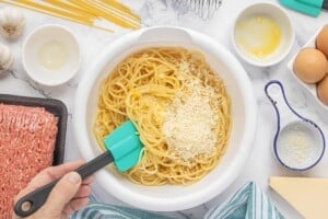 Cooked spaghetti tossed with eggs and Parmesan cheese in a large mixing bowl.