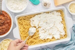 Creamy cheese mixture spread over a layer of spaghetti in a casserole dish.
