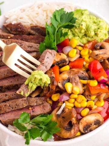 Steak bowl recipe with sliced steak, rice, sautéed mushrooms, sweet corn, bell peppers, red onion, and creamy avocado.