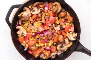 Mushrooms, corn, bell peppers, and red onion saut&eacute;ing in a cast iron skillet.