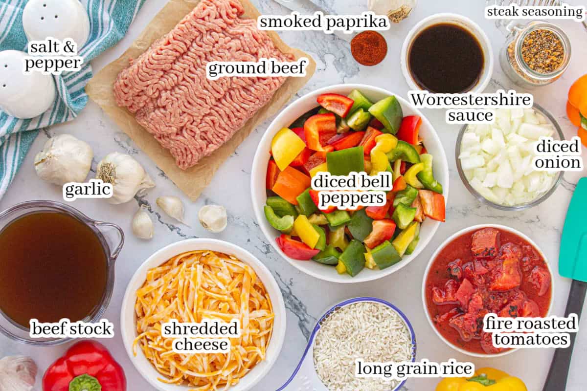 Overhead view of the ingredients for stuffed bell pepper casserole arranged on a marble surface, including ground beef, diced bell peppers, onion, garlic, beef stock, fire-roasted tomatoes, long grain rice, shredded cheese, Worcestershire sauce, smoked paprika, steak seasoning, salt, and pepper.