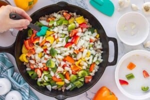 Diced bell peppers and onions added to browned ground beef in a cast iron skillet.