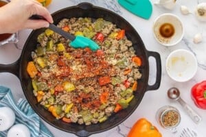 Ground beef, bell peppers, and onions cooking together in a skillet with Worcestershire sauce and seasonings added for stuffed bell pepper casserole.