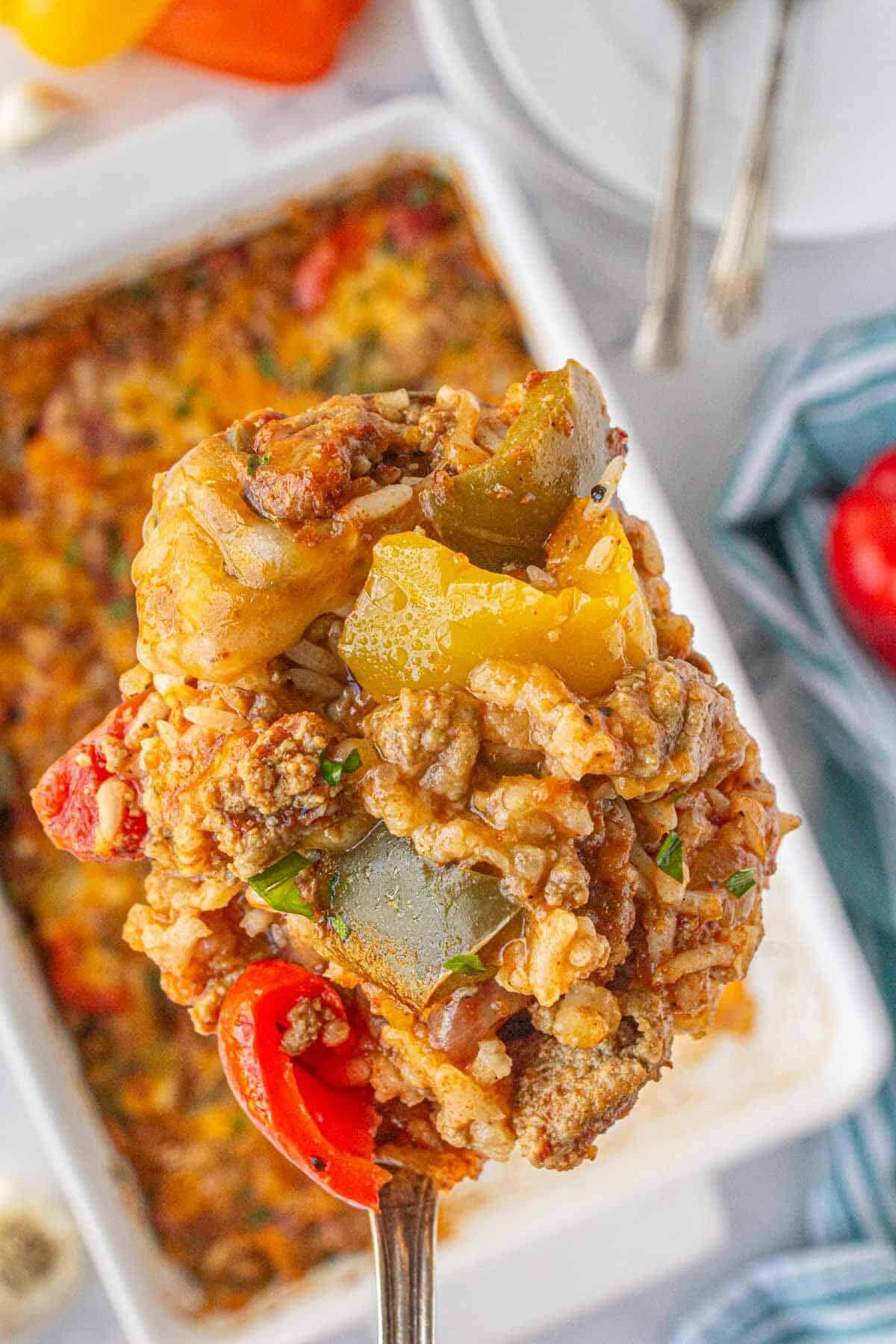 Spoon lifting a hearty bite of bell pepper casserole filled with ground beef, rice, melted cheese, and colorful bell peppers from a baking dish.