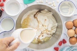 Adding milk to cake mix, pudding mix, sour cream, and eggs to make cake batter.