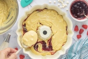 Layering White Chocolate Raspberry Bundt Cake batter over raspberry preserves in a prepared bundt pan.