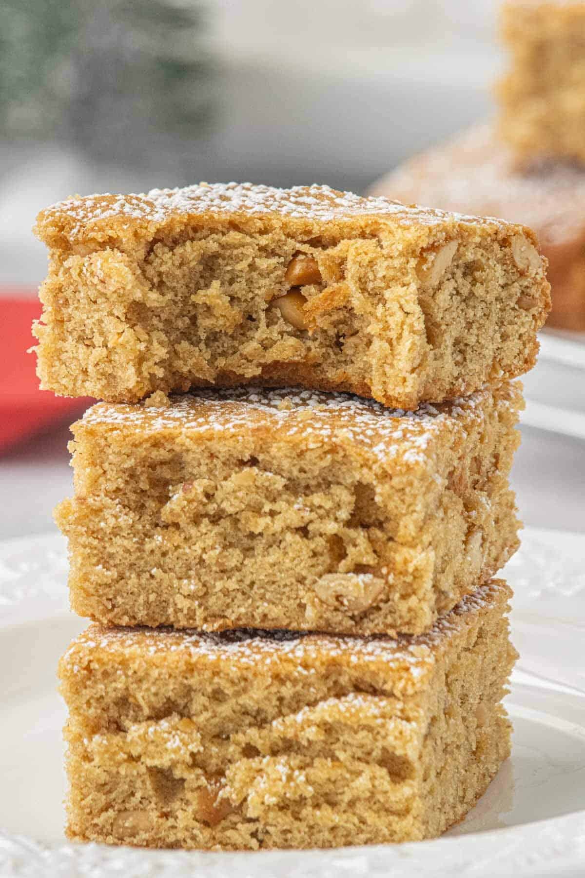Three peanut butter blondies stacked on a white plate, dusted with powdered sugar and showing the soft, chewy interior with chopped peanuts.