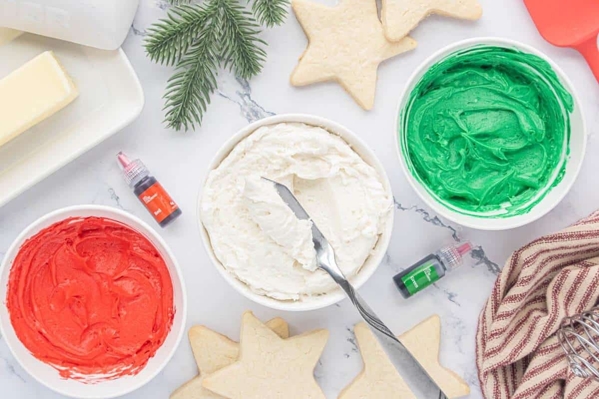 Creamy buttercream frosting color red, white and green in bowls ready for decorating cookies.