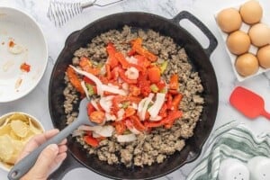 Browned breakfast sausage topped with sautéed red peppers and onions in a cast iron skillet.