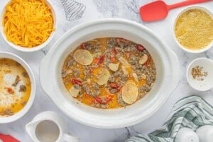 Slow cooker filled with sausage, potatoes, roasted red peppers, and egg mixture before adding cheese.