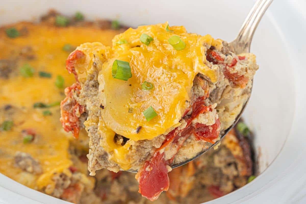 Cheesy Christmas breakfast casserole with sausage, potatoes, eggs, and roasted red peppers served on a large spoon.