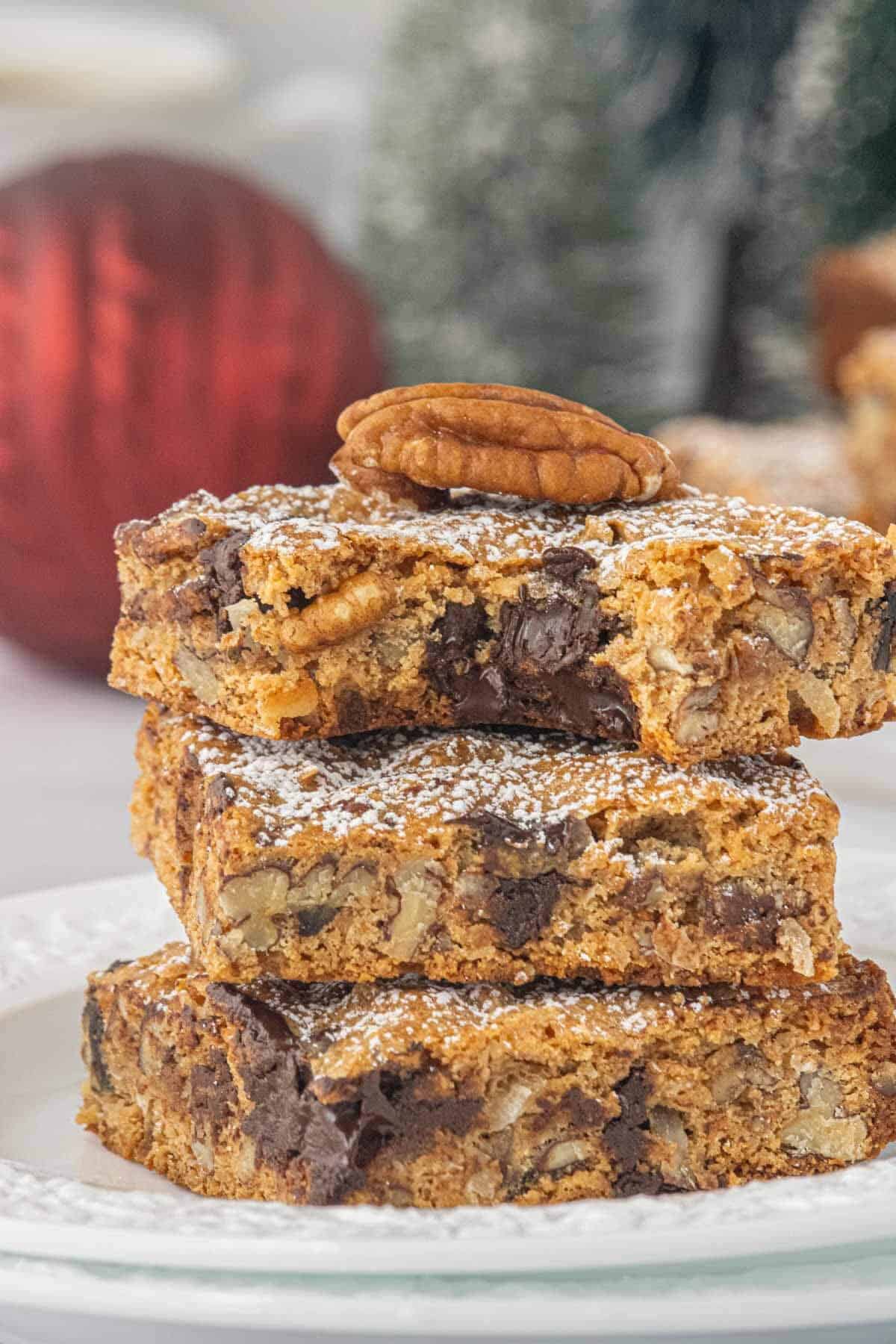 Close-up of stacked Graham Cracker Pecan Cookie Bars garnished with a whole pecan and dusted with powdered sugar. There's a bite taken out of the top bar, revealing the rich chocolate-filled interior.