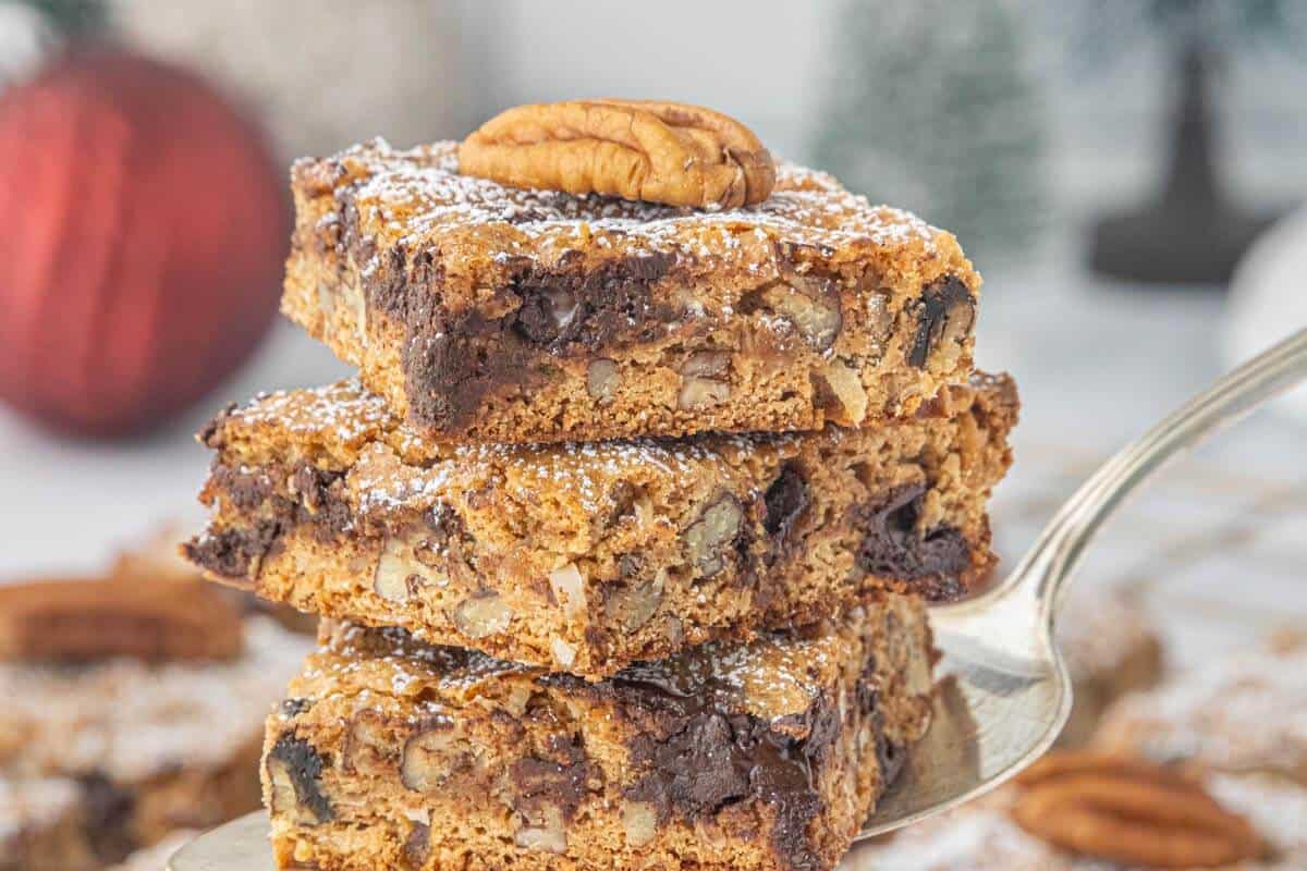Three Graham Cracker Pecan Cookie Bars stacked on a cake server, highlighting the soft texture, melted chocolate, chopped pecans, and powdered sugar topping.