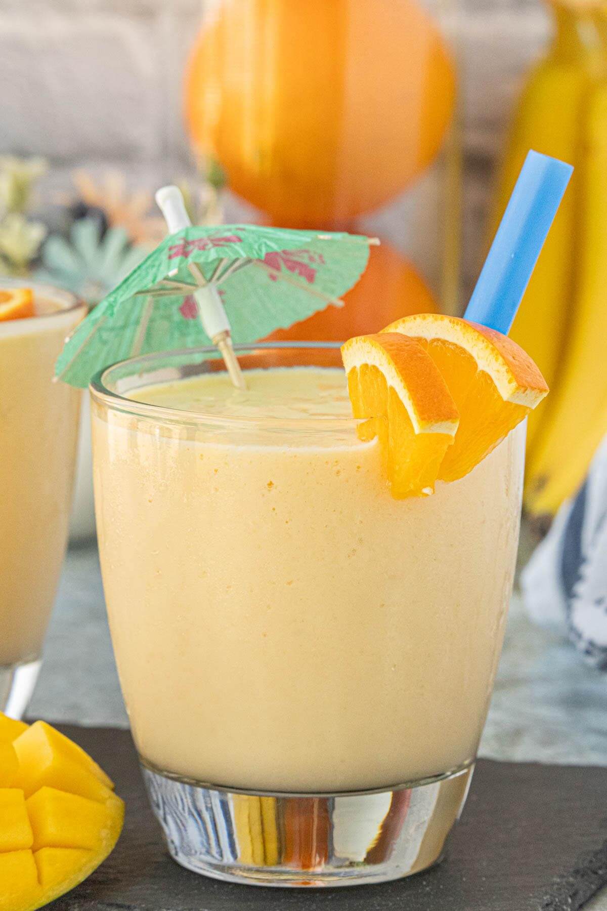 Mango Orange Creamsicle Smoothie in a glass with an orange slice garnish, tropical umbrella, and fresh mango cubes nearby.