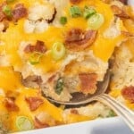 Close-up of a spoonful of Million Dollar Potato Casserole topped with melted cheddar cheese, crispy bacon, and sliced green onions.