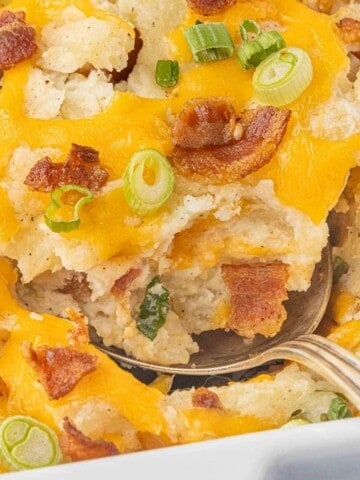Close-up of a spoonful of Million Dollar Potato Casserole topped with melted cheddar cheese, crispy bacon, and sliced green onions.