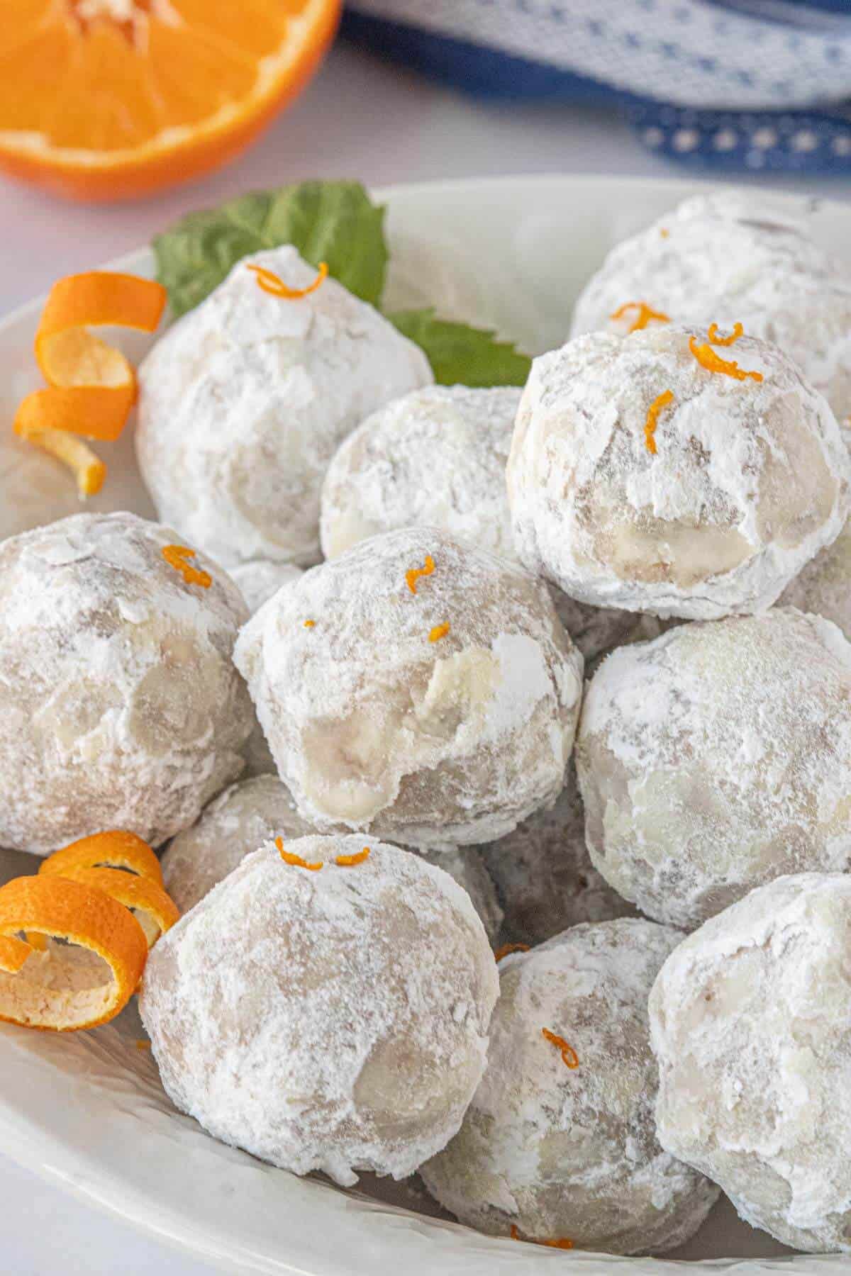 Close-up of Orange Snowballs coated in powdered sugar, garnished with orange zest, and served in a white bowl.