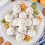 An overhead shot of a serving bowl filled with Orange Snowballs dusted with powdered sugar and garnished with fresh orange zest and mint leaves.