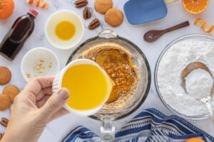 Pouring melted butter into crushed vanilla wafers, orange zest, pecans, and orange juice concentrate in a mixing bowl.