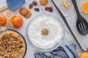 Rolling an Orange Snowball cookie ball in powdered sugar before placing it on a parchment-lined baking sheet.