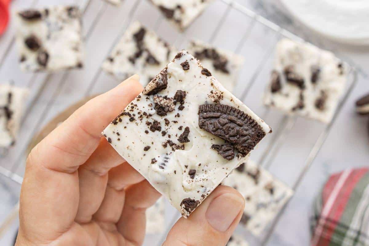 Hand holding a square of three-ingredient Oreo fudge topped with chopped Oreo cookie pieces.