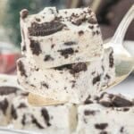 Close-up of two pieces of creamy Oreo fudge stacked on a serving spatula, showing chunks of Oreo cookies throughout.