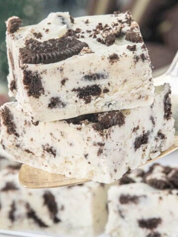Close-up of two pieces of creamy Oreo fudge stacked on a serving spatula, showing chunks of Oreo cookies throughout.