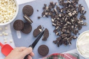 Hand chopping Oreo cookies into small pieces on a cutting board.