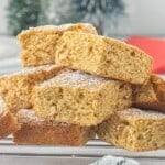 Stacked peanut butter blondies dusted with powdered sugar on a cooling rack, showing their soft, chewy texture and chopped peanuts throughout.