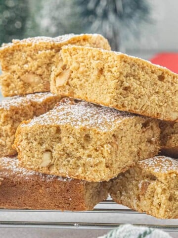 Stacked peanut butter blondies dusted with powdered sugar on a cooling rack, showing their soft, chewy texture and chopped peanuts throughout.