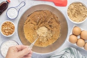 Brown sugar is being added to a mixing bowl with creamed peanut butter and butter.
