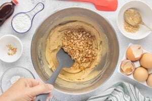 Chopped peanuts are folded into thick peanut butter blondie batter with a silicone spatula.