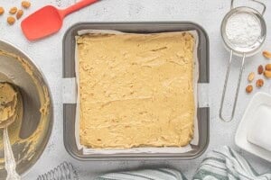 Blondie batter is spread evenly into a parchment-lined square baking pan, ready to bake.