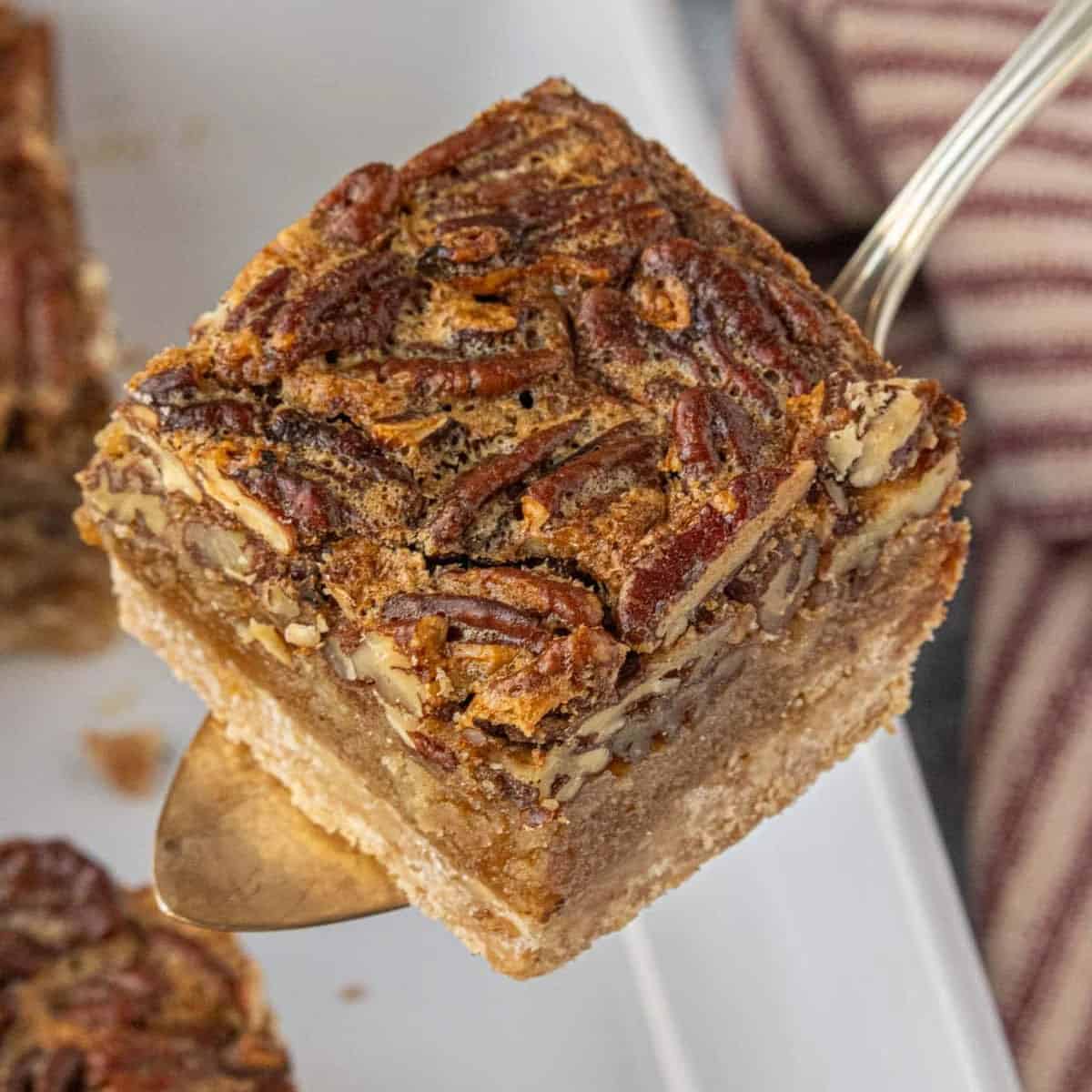 Close-up of a brown butter pecan pie bar with a buttery shortbread crust and gooey pecan filling, served on a dessert server.