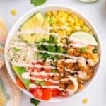 Shrimp burrito bowl with seasoned shrimp, rice, avocado, tomatoes, corn, cilantro, and creamy lime dressing in a white bowl.