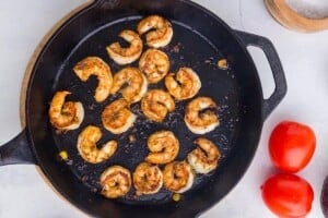 Seasoned shrimp cooking in a hot cast iron skillet until lightly browned and cooked through.