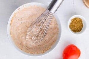 Creamy lime dressing made with sour cream, lime juice, and seasonings being whisked together in a white bowl.
