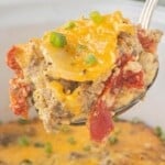 Close-up of a spoonful of slow cooker Christmas breakfast casserole with sausage, potatoes, eggs, roasted red peppers, and cheddar cheese.