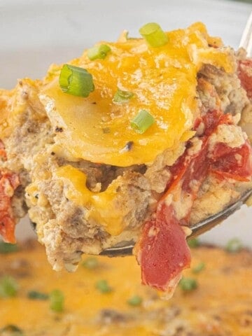Close-up of a spoonful of slow cooker Christmas breakfast casserole with sausage, potatoes, eggs, roasted red peppers, and cheddar cheese.
