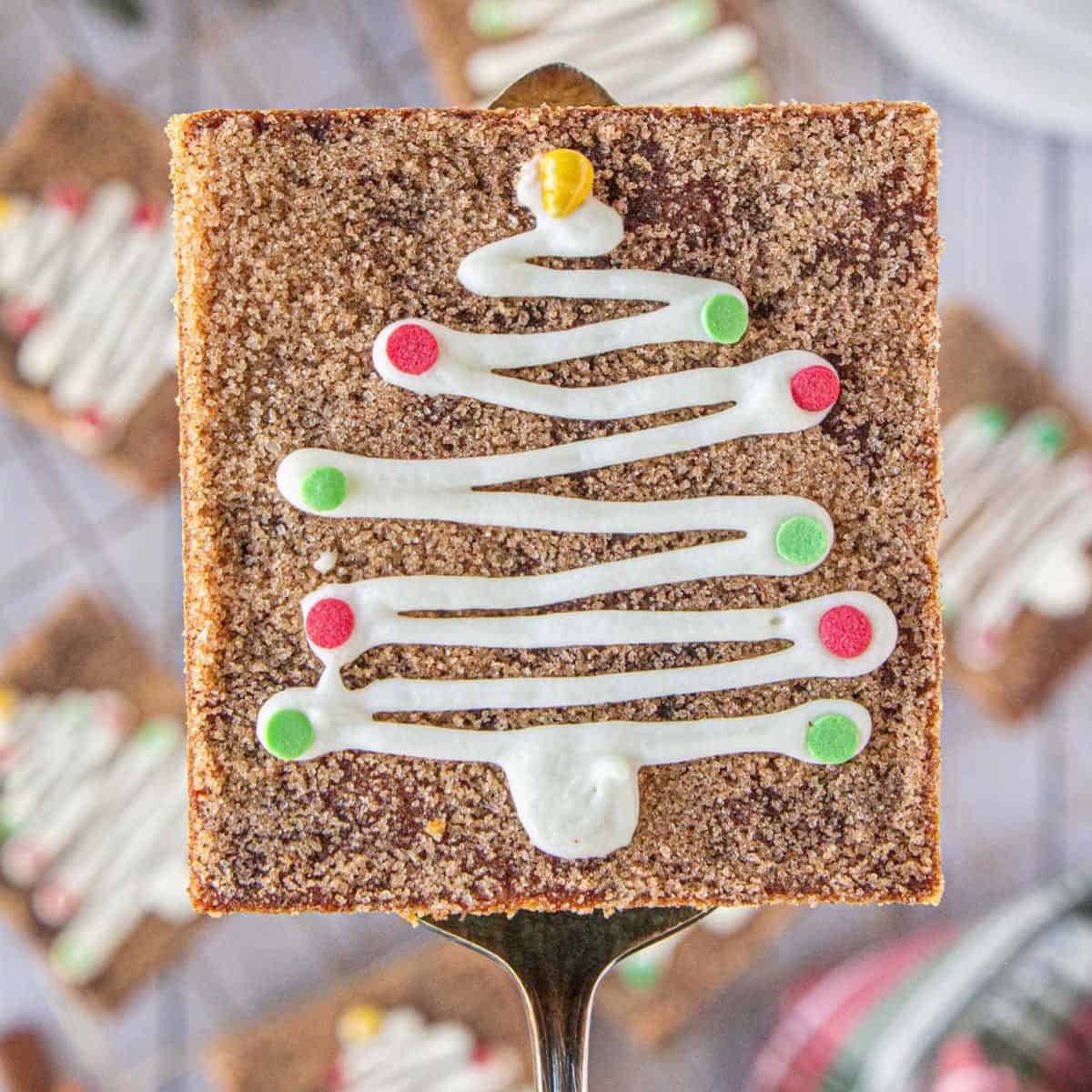 Square snickerdoodle cookie bar coated in cinnamon sugar and decorated with a white icing Christmas tree and colorful candy ornaments, served on a dessert server.
