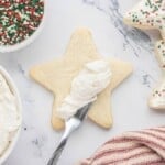 Spreading homemade buttercream sugar cookie frosting onto a star-shaped sugar cookie.