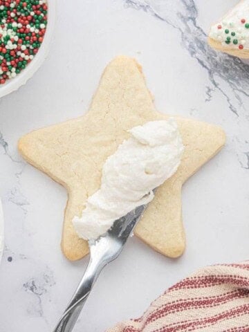 Spreading homemade buttercream sugar cookie frosting onto a star-shaped sugar cookie.