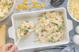 Creamy chicken and broccoli pasta mixture being spooned into a prepared baking dish.