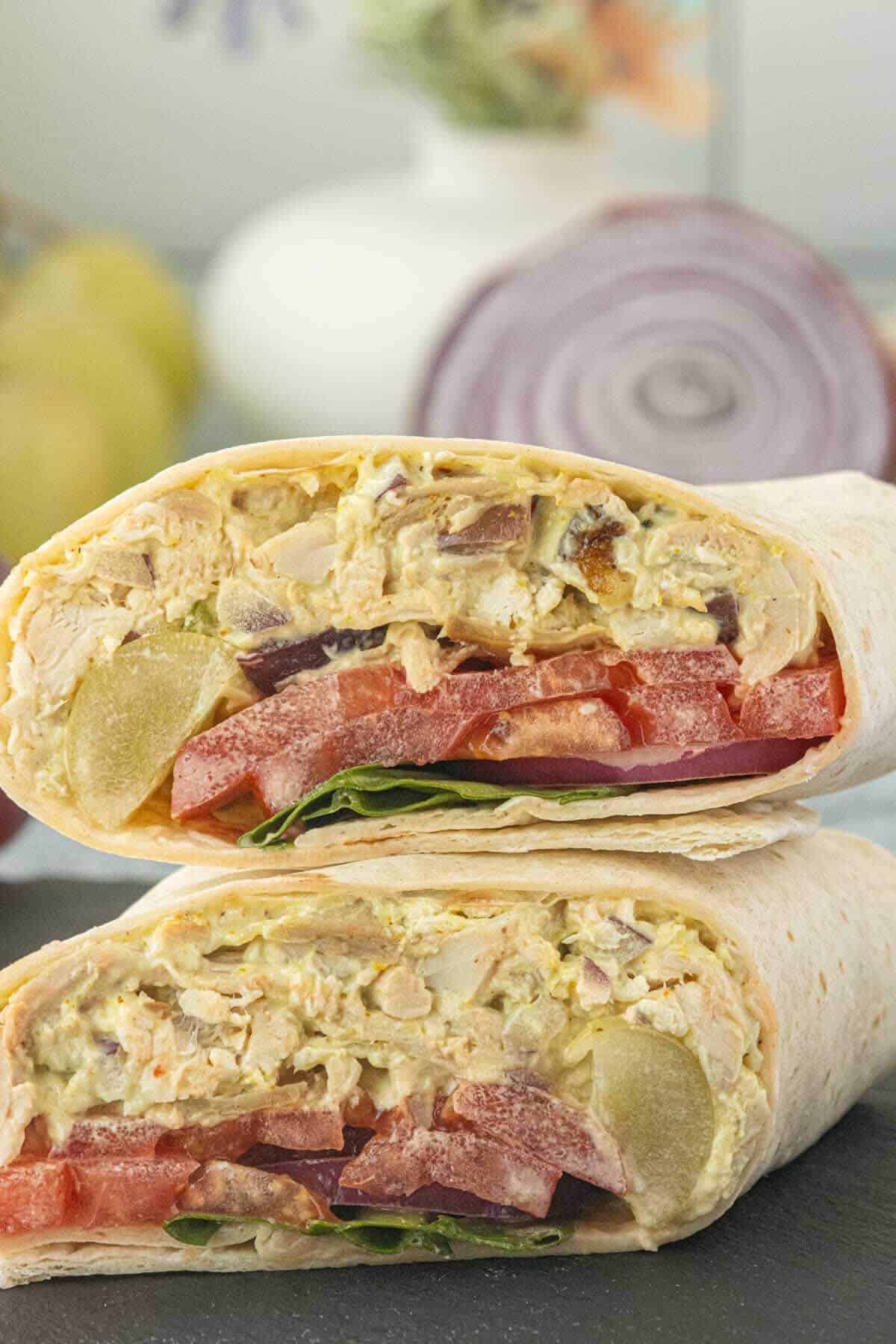 Curry chicken salad wraps filled with grapes, tomatoes, red onion, and fresh spinach, sliced in half and stacked for serving.